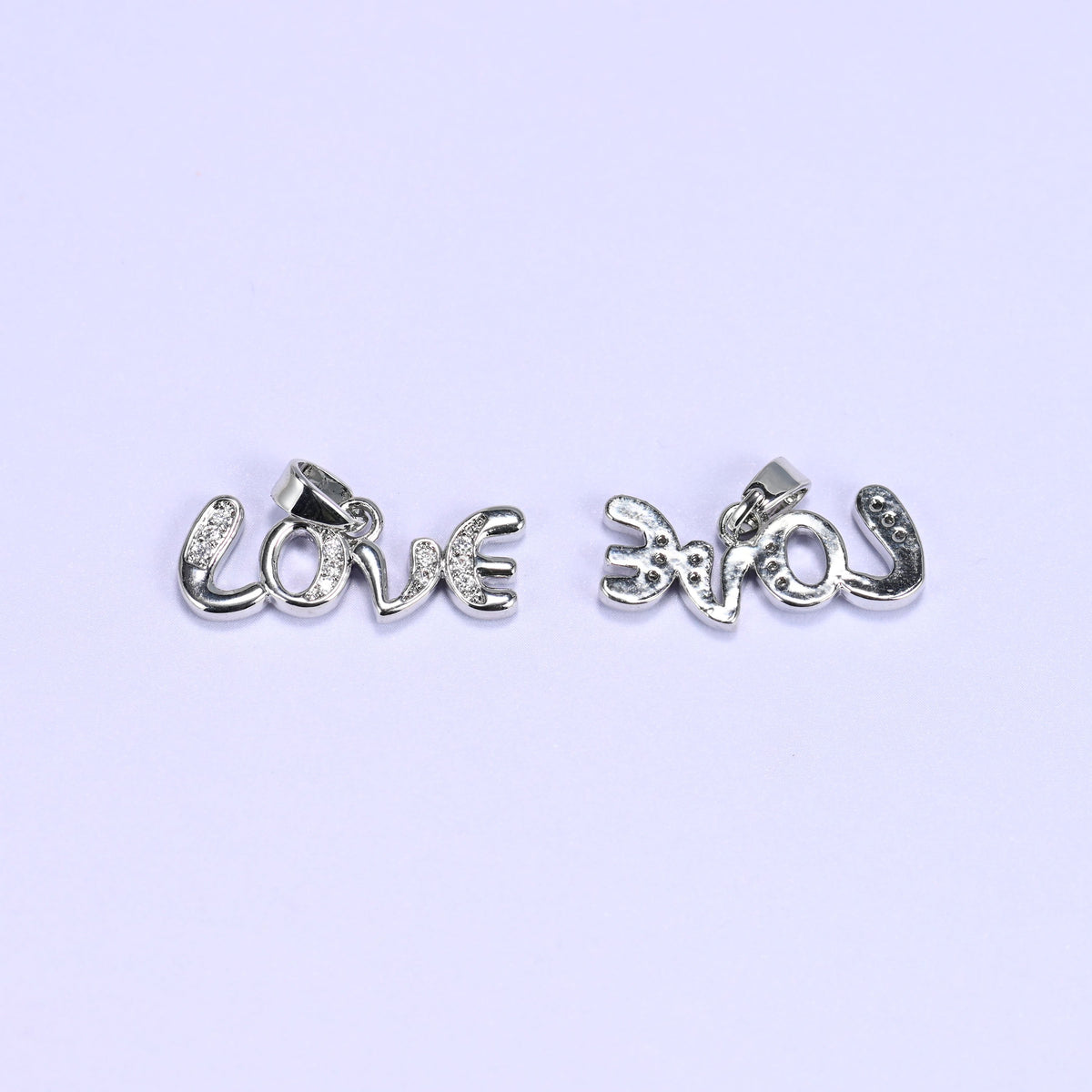 Silver-tone Love letter zirconia charms, one pendant face up and one turned over to show the smooth reverse side.