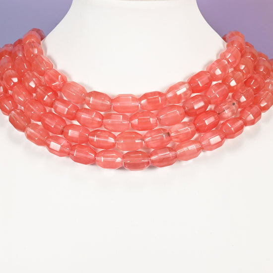 Multi-strand necklace of coral pink glass barrel beads laid on a white mannequin neck form against a lavender background.