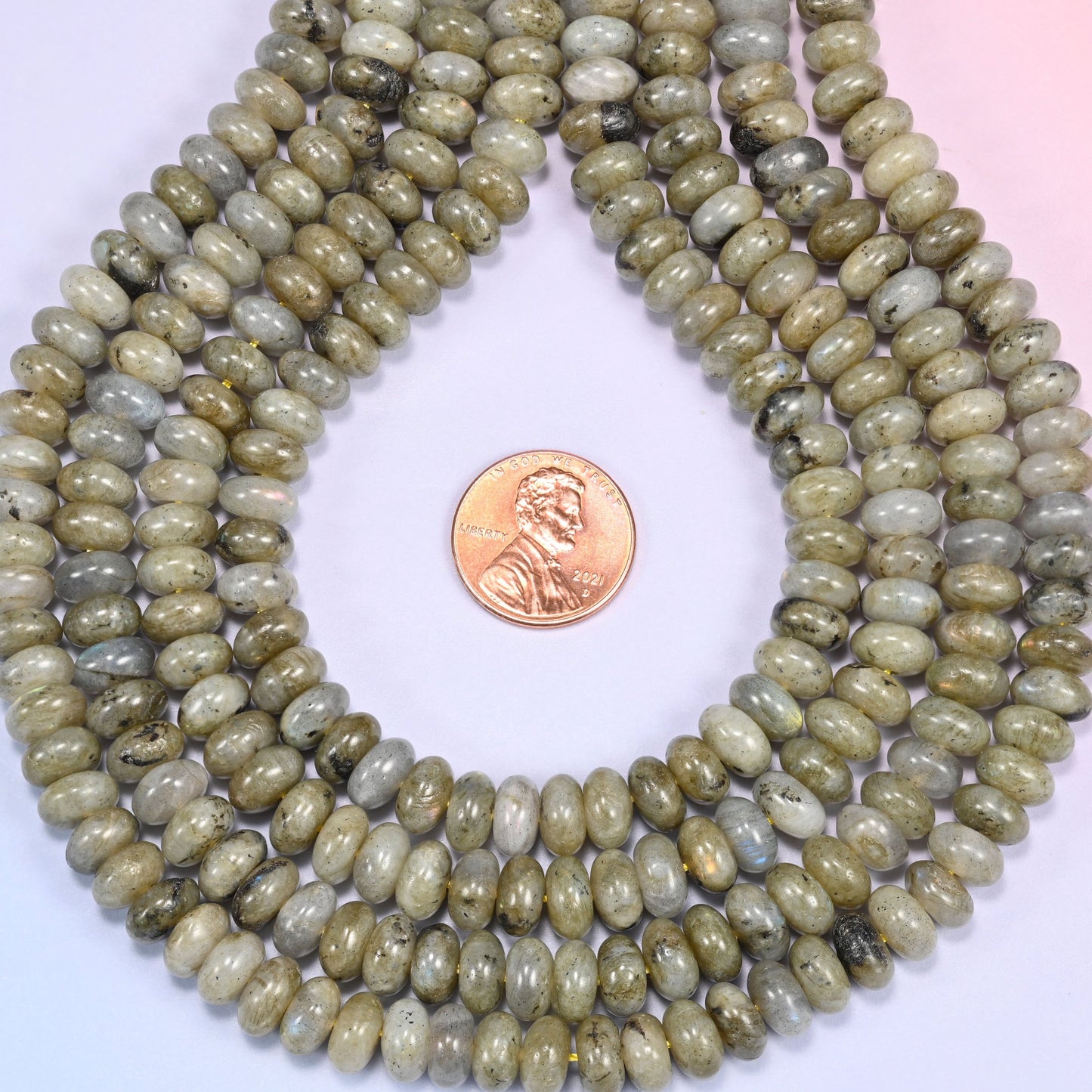 Bundled coil of Grey Labradorite rondelle beads on a lavender background with a penny placed at the center for scale.