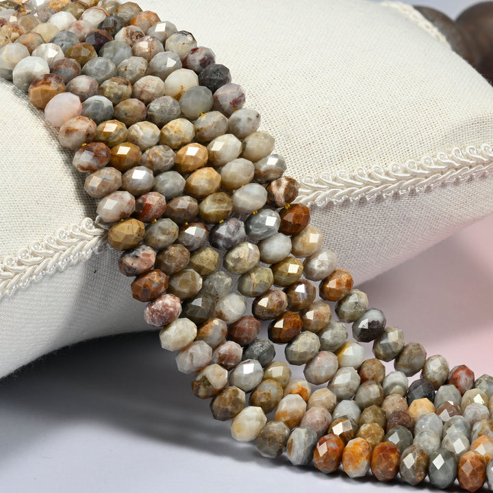 Gobi desert agate faceted rondelle beads 5x8mm in gray, cream and golden tan, several strands draped over a white cushion