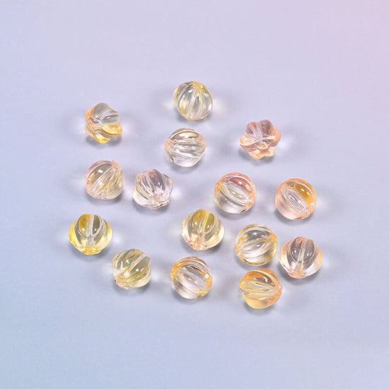 A scattered group of loose 8mm yellow clear pumpkin glass beads, showing the melon ribs and the drill holes.