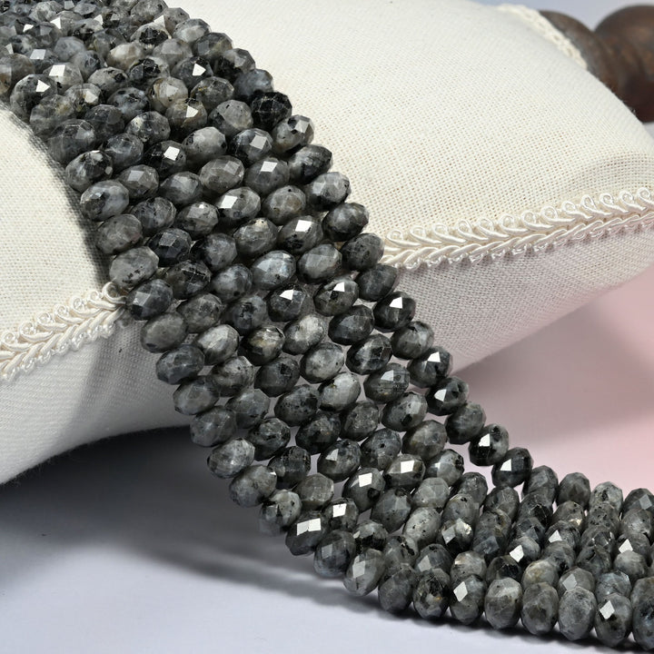 Black labradorite faceted rondelle beads 5x8mm in smoky charcoal gray speckled with black, several strands draped over a white cushion