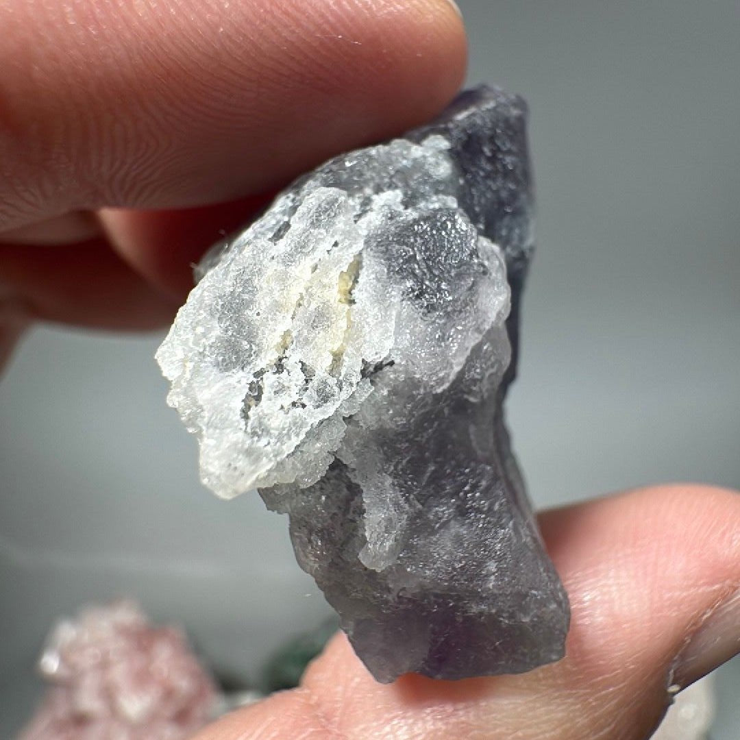 Narrow edge-on view of the fluorite wedge held between two fingers, showing its slim profile