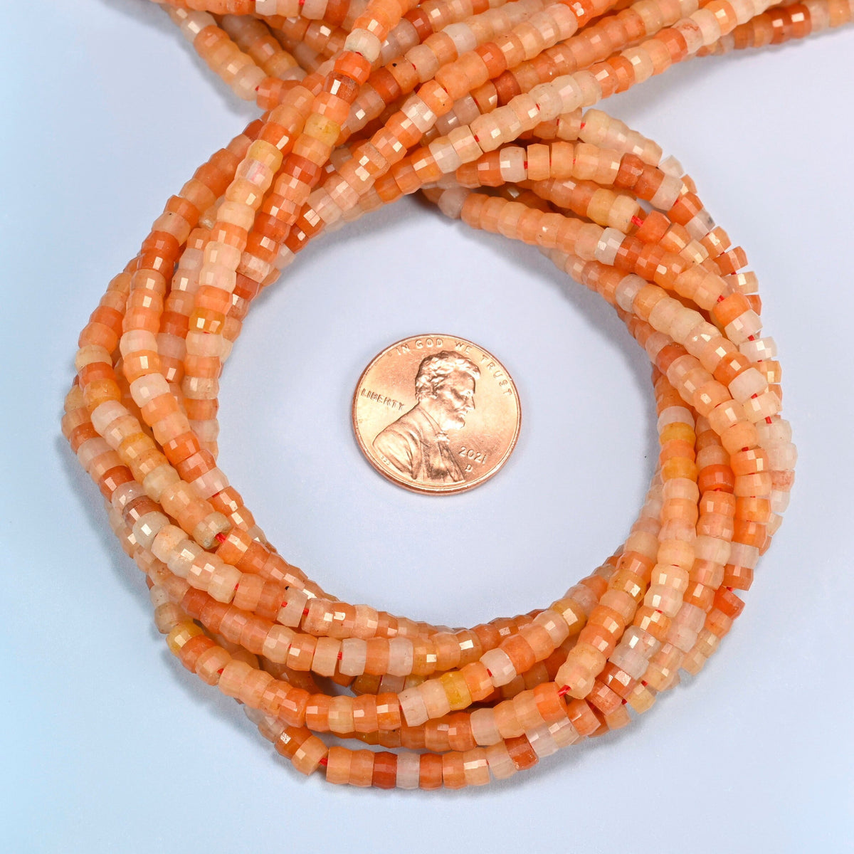 Red aventurine faceted heishi disc beads 2x4mm coiled in a loop around a US penny for scale, close-up of the faceted disc shape