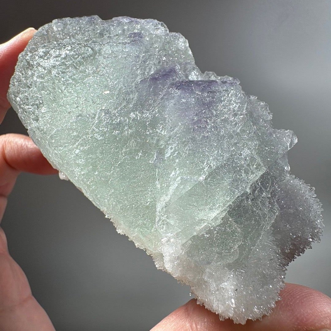 Green fluorite specimen held in hand, pale mint body stepping down in natural cube faces under a frosted quartz crust