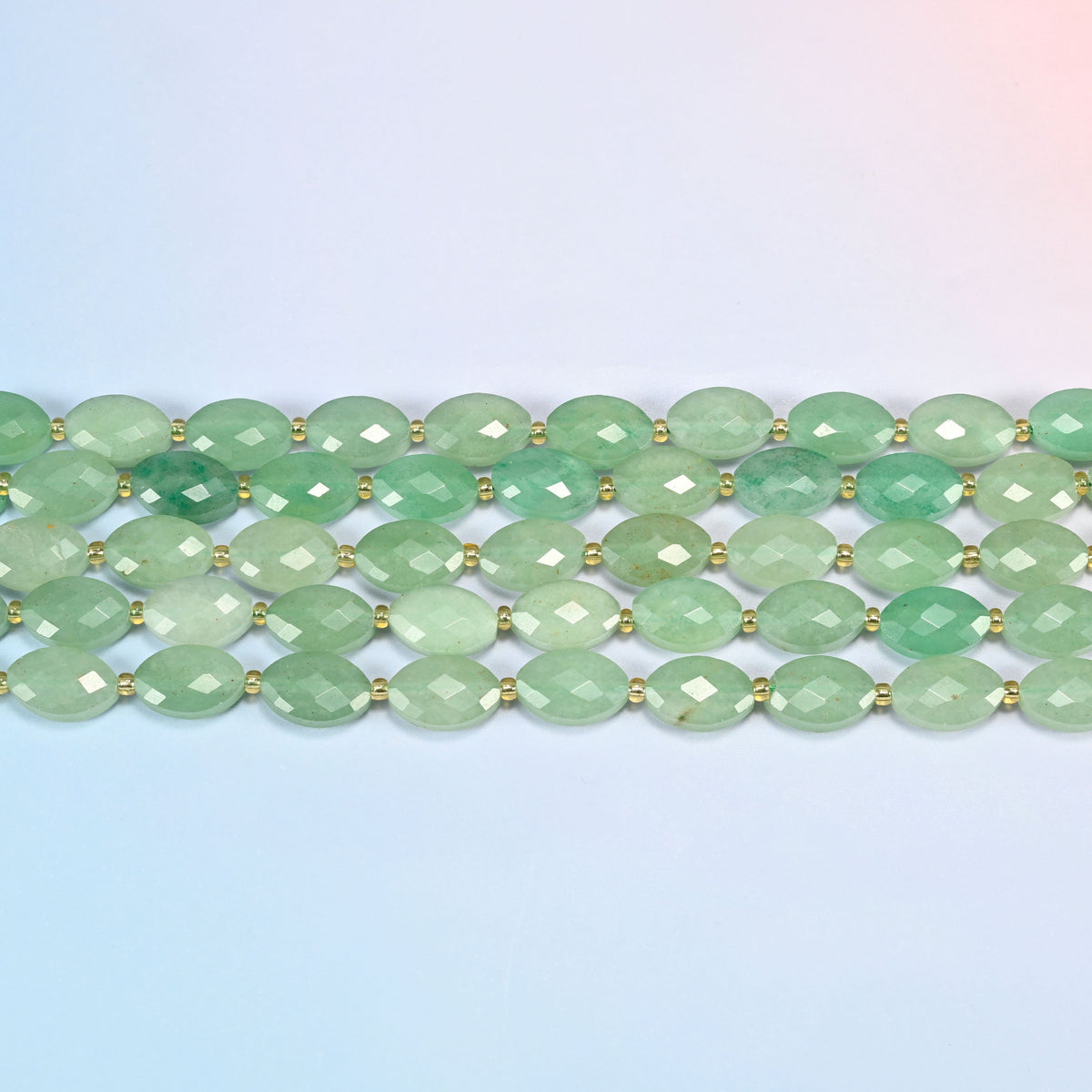 Several strands of green aventurine faceted flat oval beads laid in straight rows with gold seed bead spacers