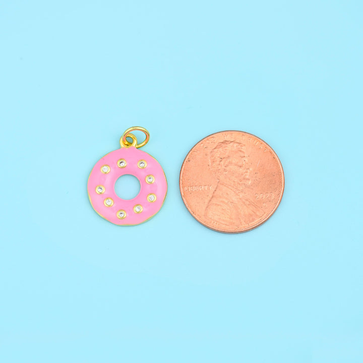 Enamel donut charm in pink shown beside a US penny, the glazed ring a little smaller than the coin.