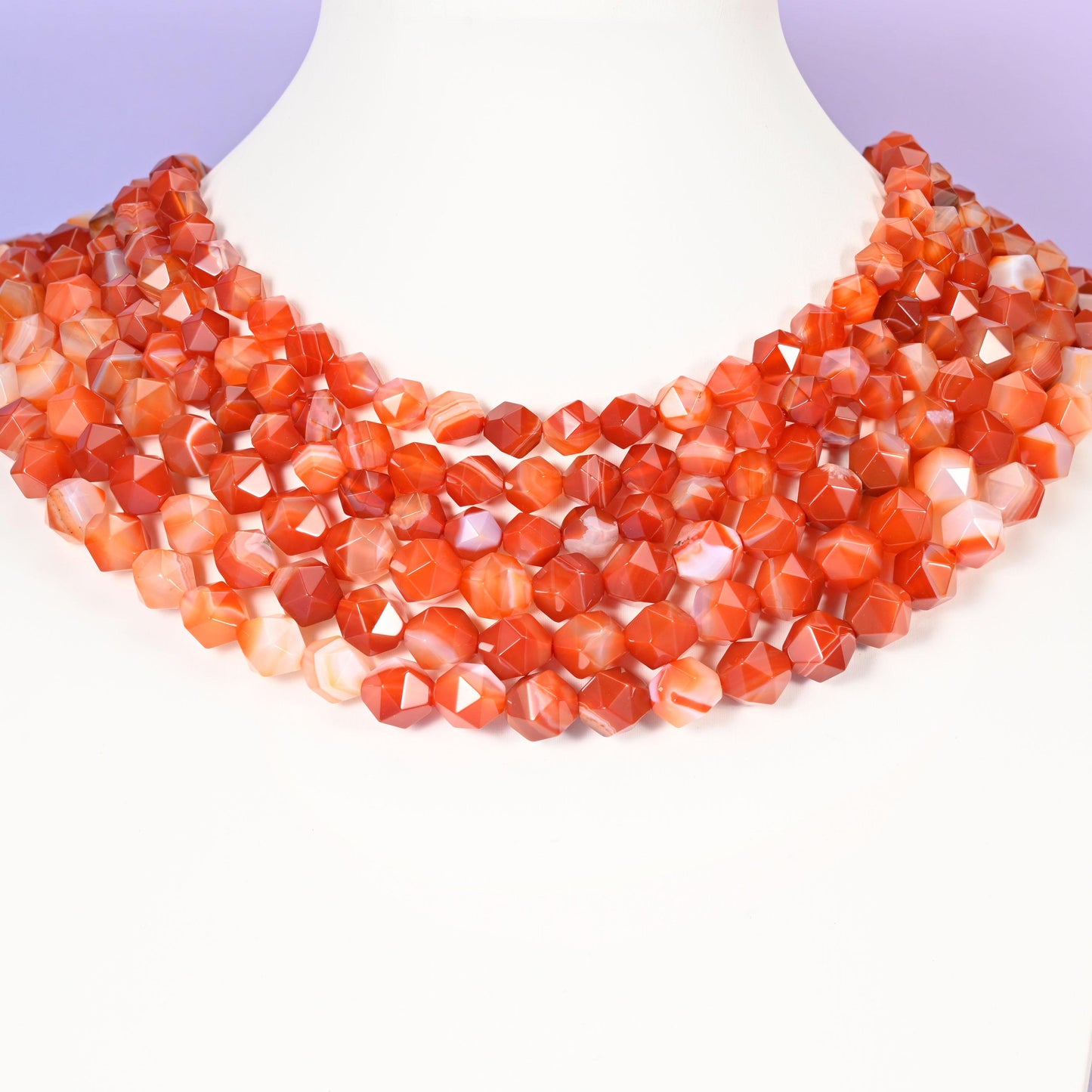 Dyed Red Stripe Agate star cut beads looped around a white neck form, several strands sitting together as a collar