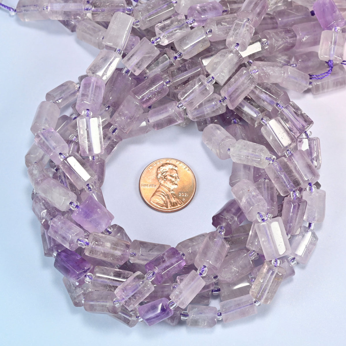 Lavender amethyst faceted tube beads wound in a ring around a US penny, close view of the faceted tube shape.