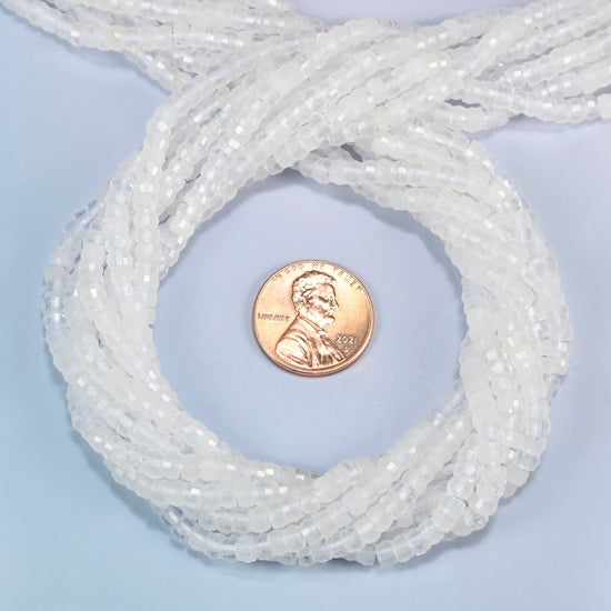 Clear quartz faceted heishi disc beads 2x4mm coiled in a loop around a US penny for scale, close-up of the faceted disc shape