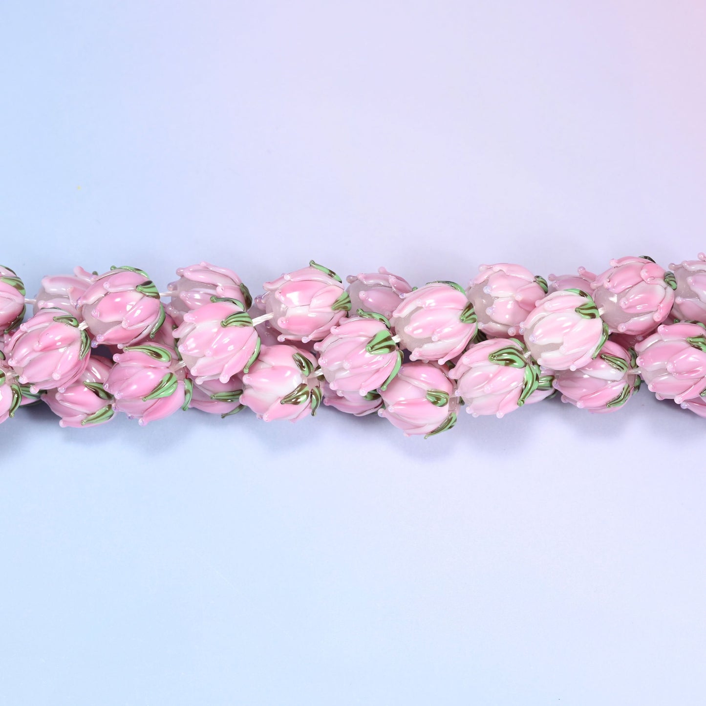 Pink tulip bud-shaped lampwork glass beads, hand-formed with sculpted petal detailing that gives a realistic flower bud look, accented with a green leaf detail at the base.