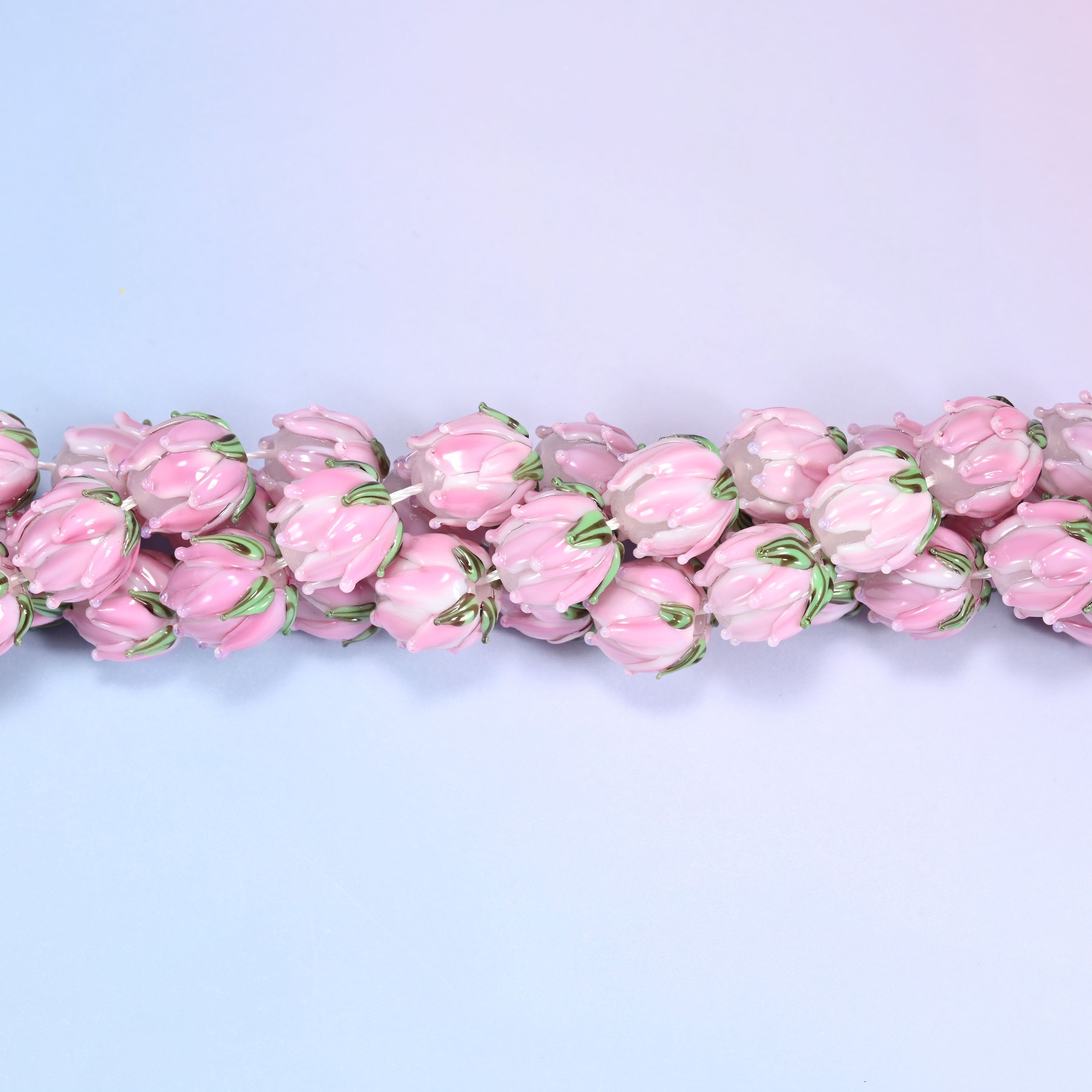 Pink tulip bud-shaped lampwork glass beads, hand-formed with sculpted petal detailing that gives a realistic flower bud look, accented with a green leaf detail at the base.