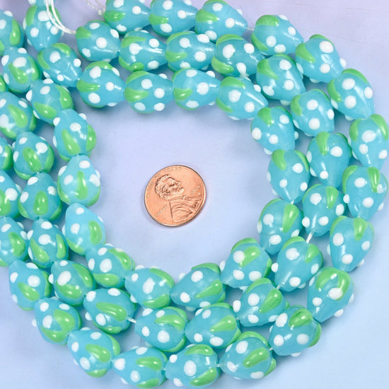 Sky blue opaque glass ovals scattered with small white seed dots and capped with an apple-green leafy band, so every bead reads as a little blue strawberry.