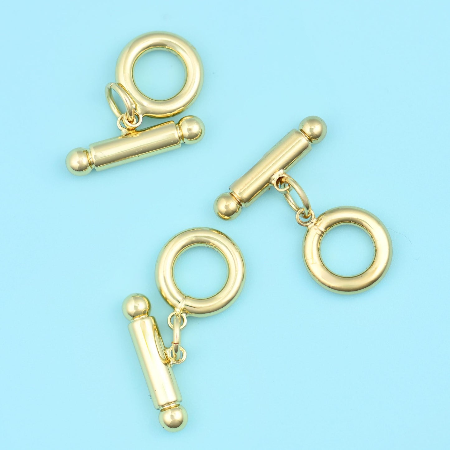 A plain polished ring paired with a slim bar that has a small ball at each end, both in warm gold, with a short jump ring…