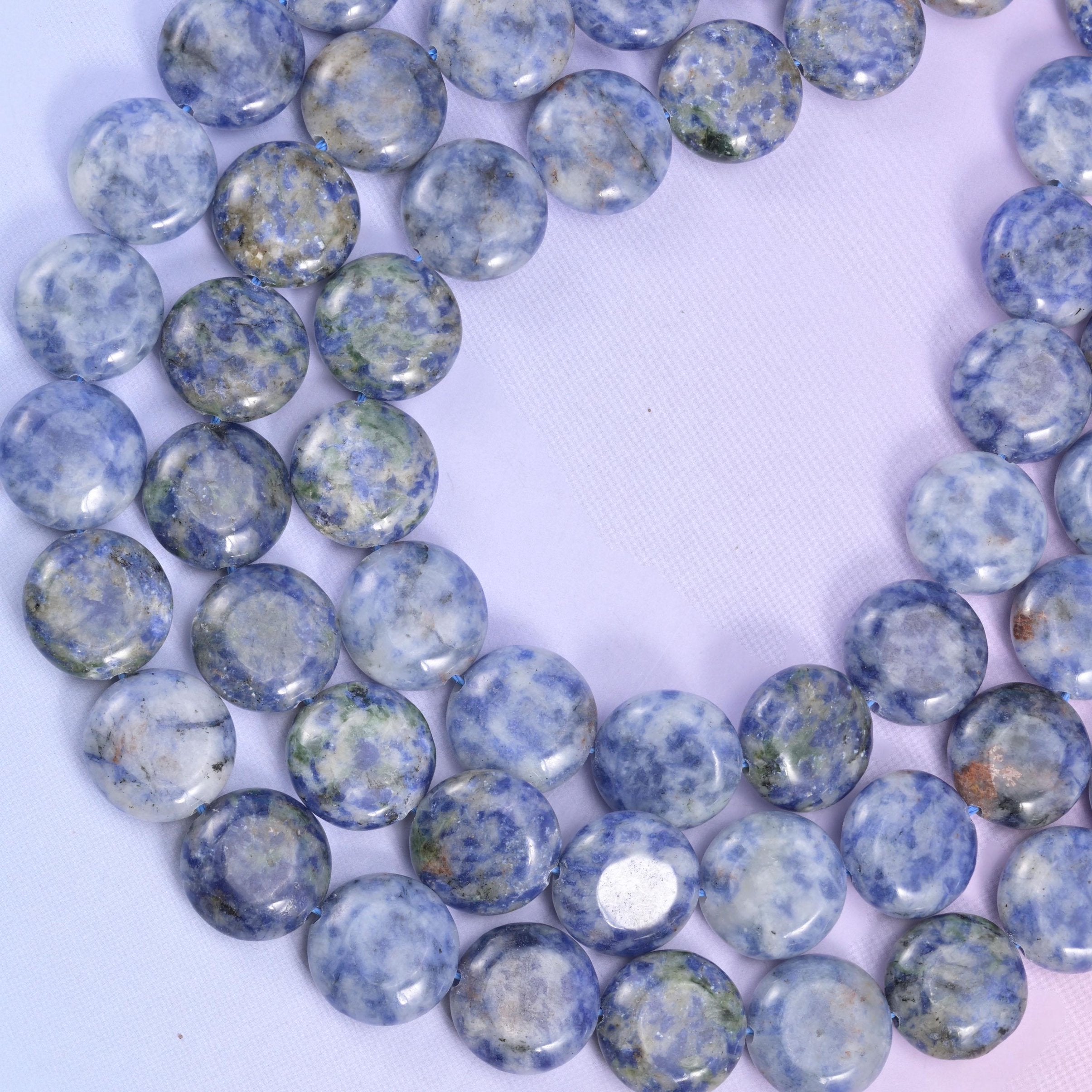 Blue spot jasper strand curled into a loop, the spotting pattern changing from bead to bead