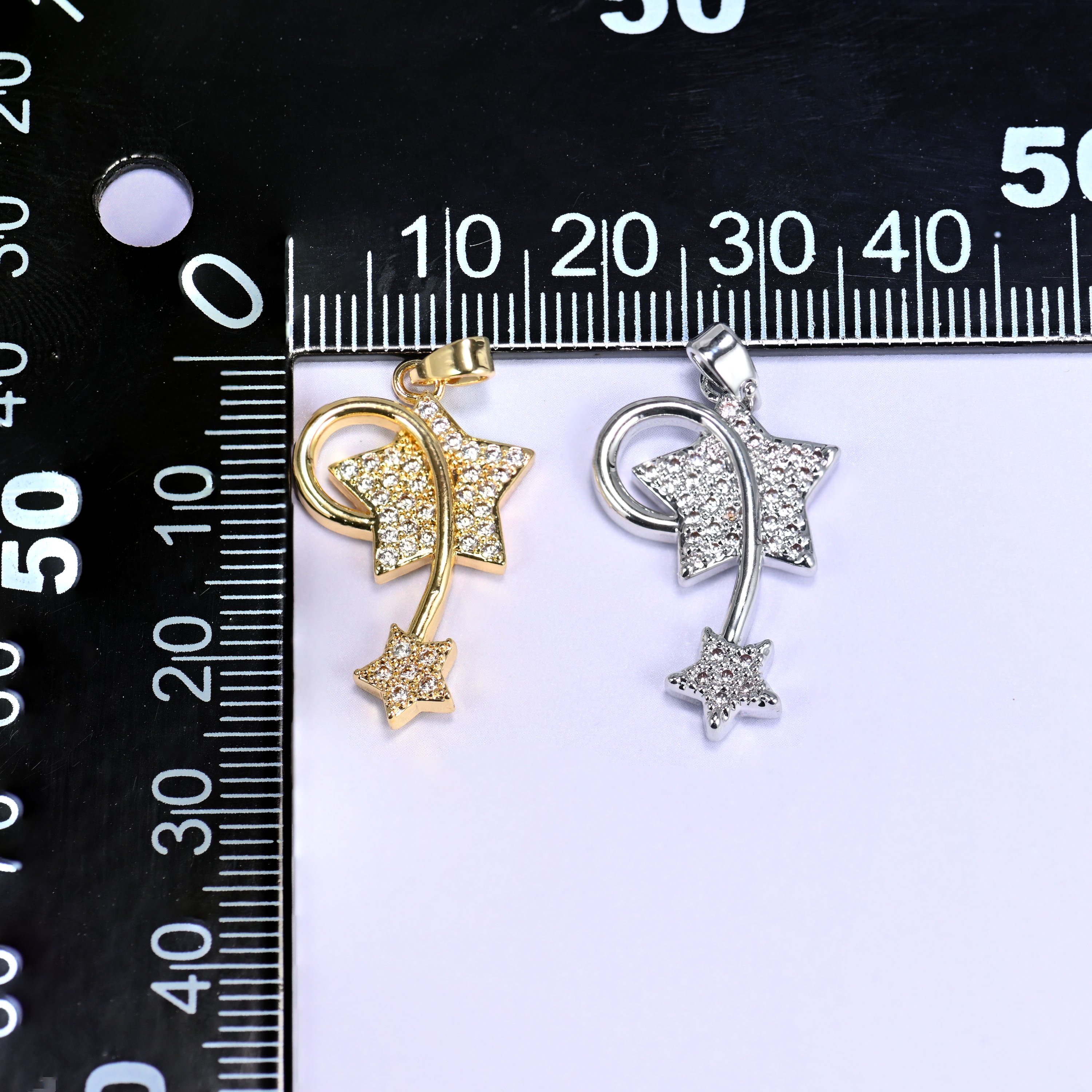 Gold and silver wishing star zirconia charms together on a black millimetre ruler for size reference.