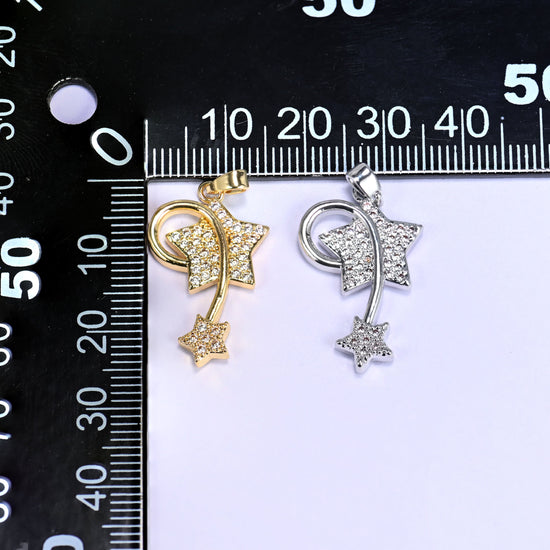 Gold and silver wishing star zirconia charms together on a black millimetre ruler for size reference.