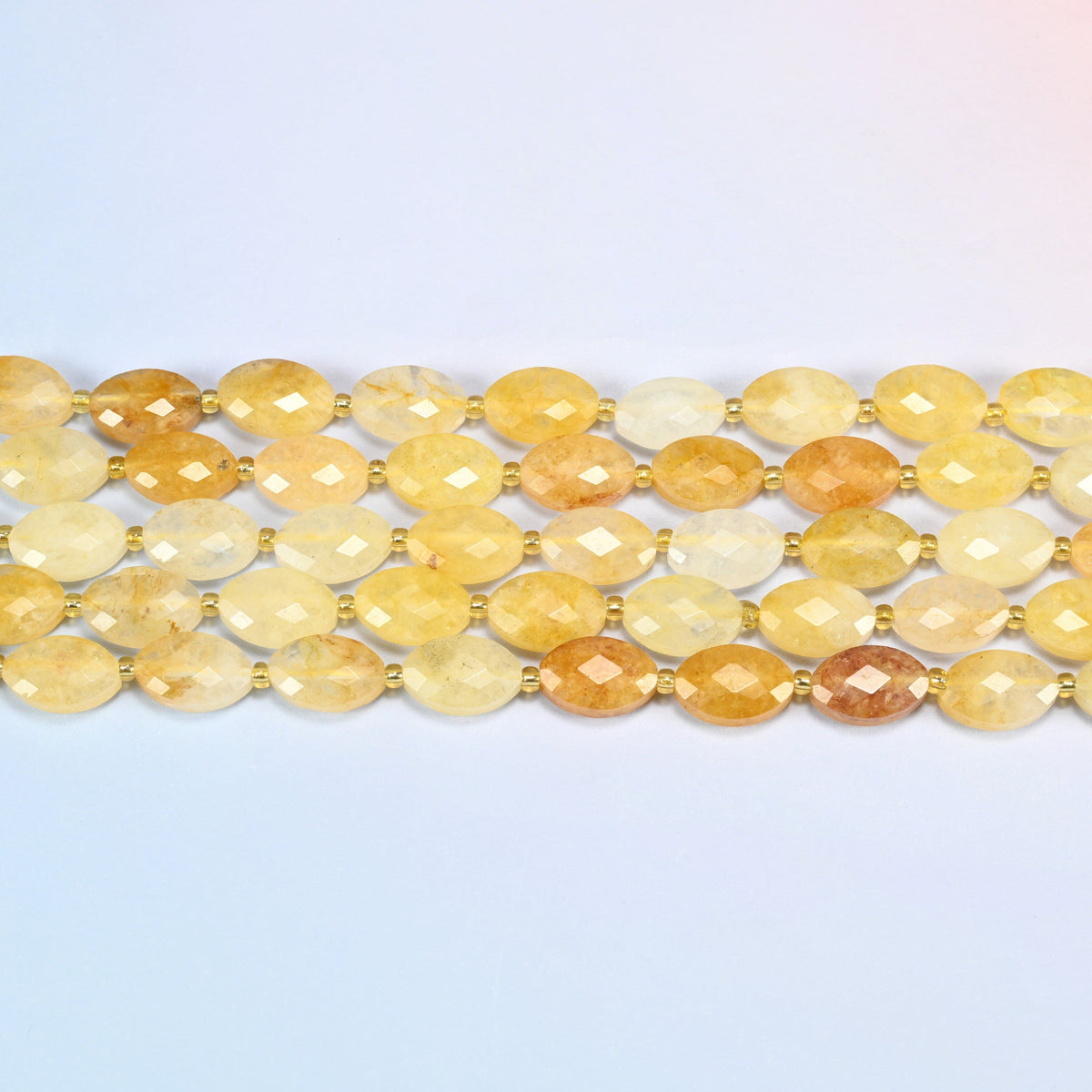 Several strands of golden healer quartz faceted flat oval beads laid in straight rows with gold seed bead spacers