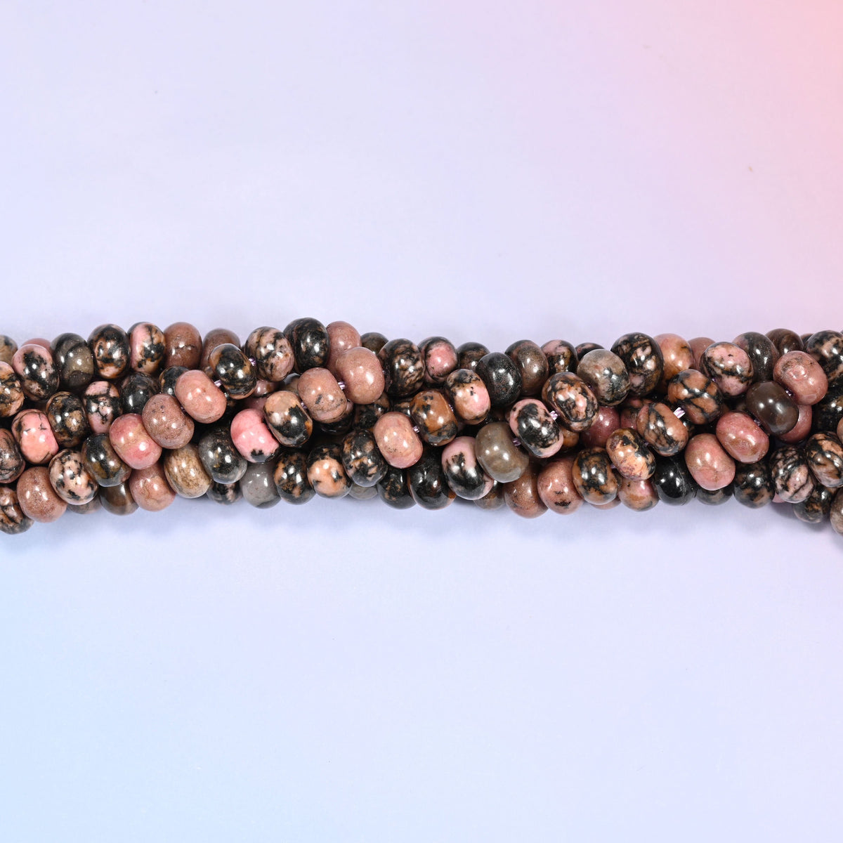 Natural Rhodonite rondelle beads in rich pink and rose tones with black manganese veining and brown patches.