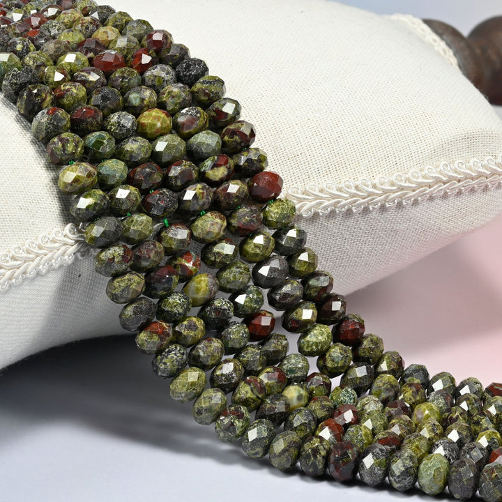 Dragon bloodstone faceted rondelle beads 5x8mm in mossy olive green splashed with oxblood red, several strands draped over a white cushion