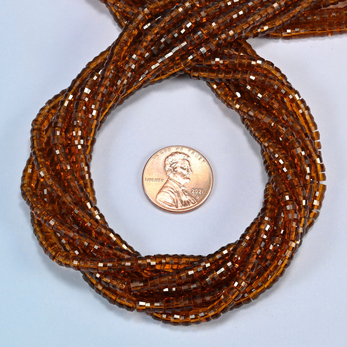 Brown glass faceted heishi disc beads 2x4mm coiled in a loop around a US penny for scale, close-up of the faceted disc shape