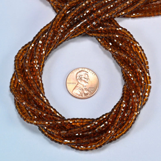 Brown glass faceted heishi disc beads 2x4mm coiled in a loop around a US penny for scale, close-up of the faceted disc shape