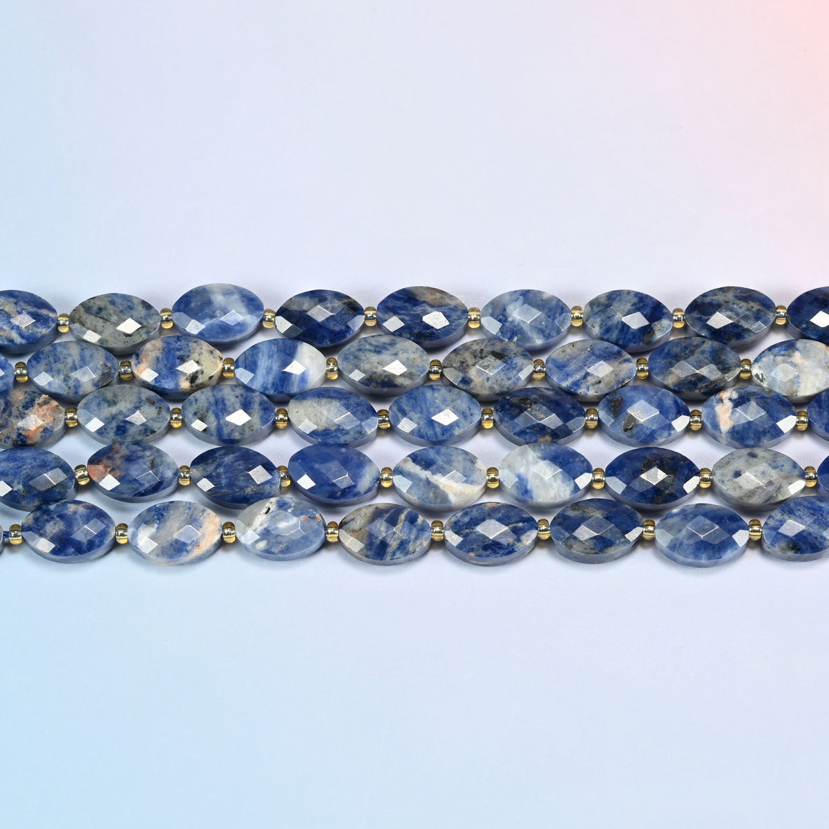 Several strands of orange sodalite faceted flat oval beads laid in straight rows with gold seed bead spacers