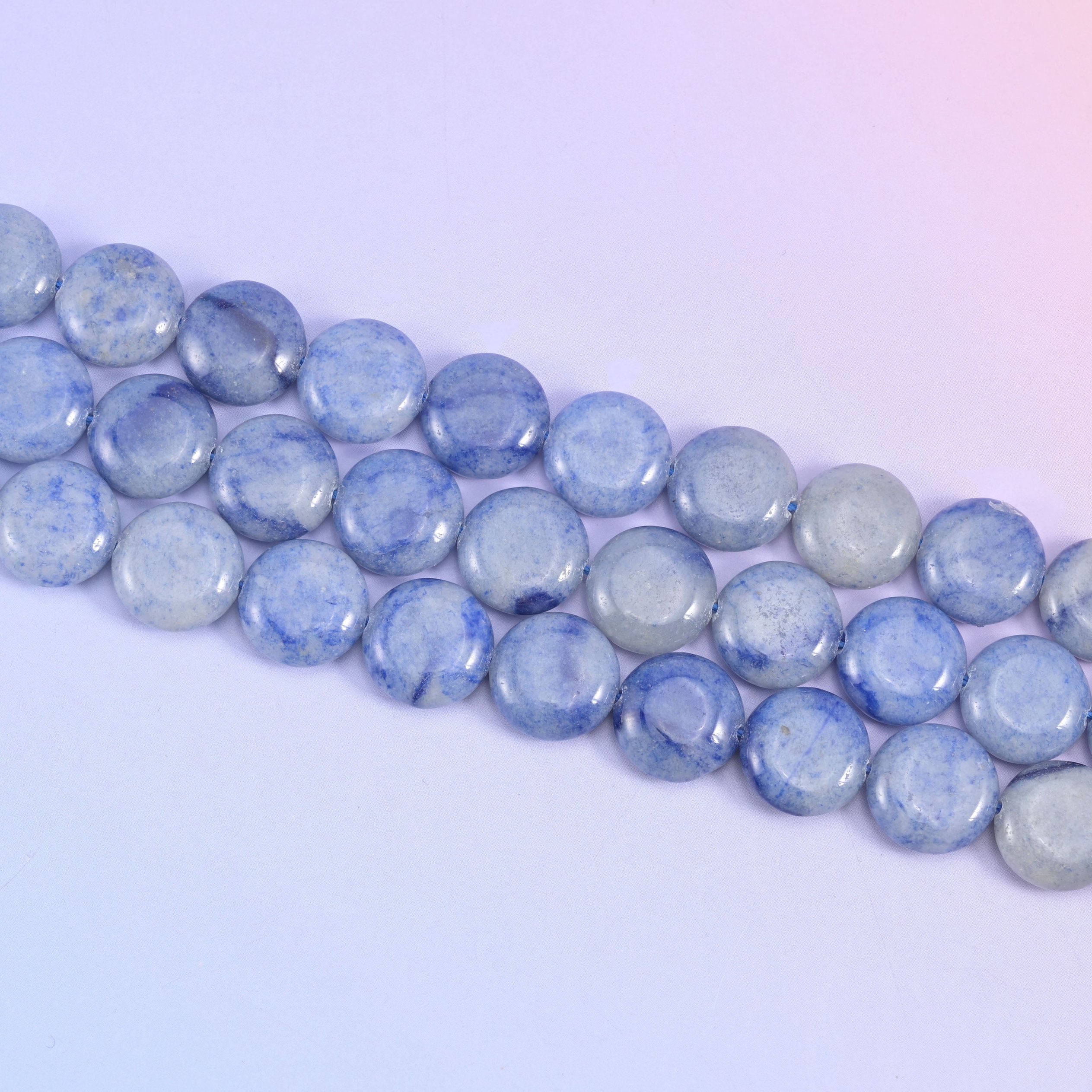 Diagonal run of blue aventurine coins across a pale backdrop, cloudy white patches breaking up the blue