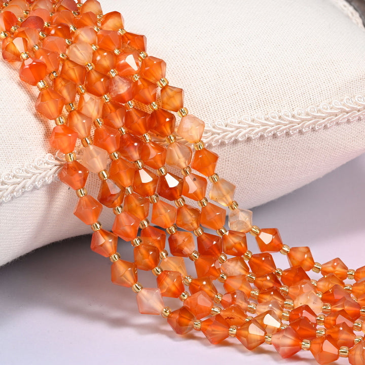 Orange carnelian faceted bicone beads with gold glass seed bead spacers draped over a white linen cushion.