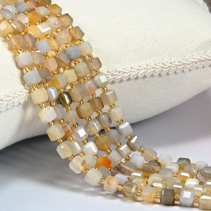 Yellow agate faceted cube beads 6mm with small gold spacer beads, several strands draped over a white cushion