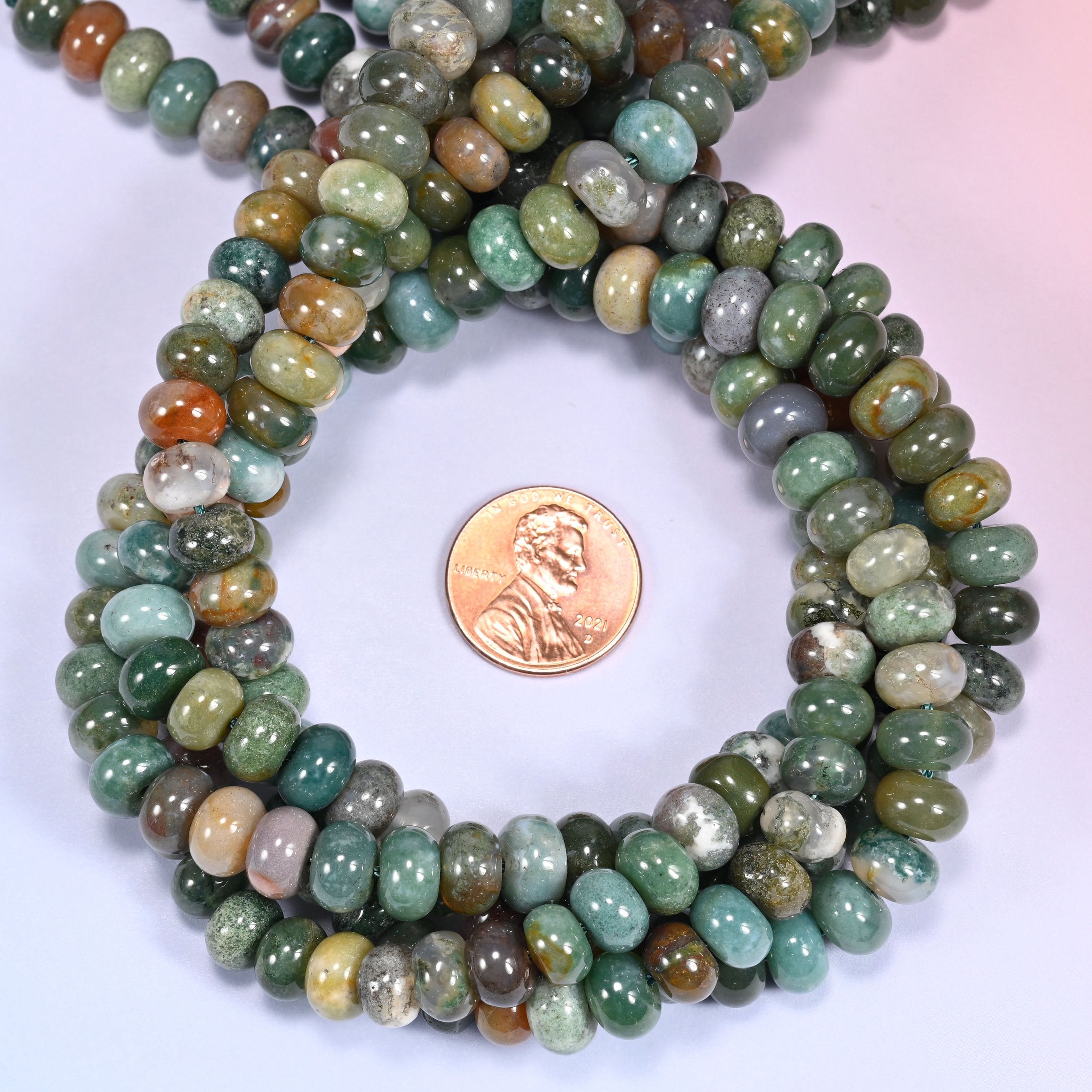 Multiple strands of Indian Agate beads gathered together on a lavender surface, loose ends visible.