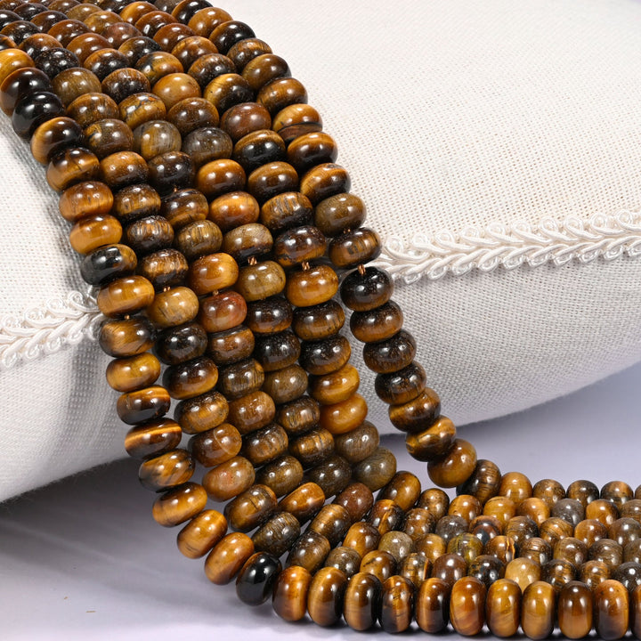 Close-up of multiple strands of polished Tiger Eye rondelle beads in golden brown and dark chocolate tones, draped over a cream fabric jewelry display bust.