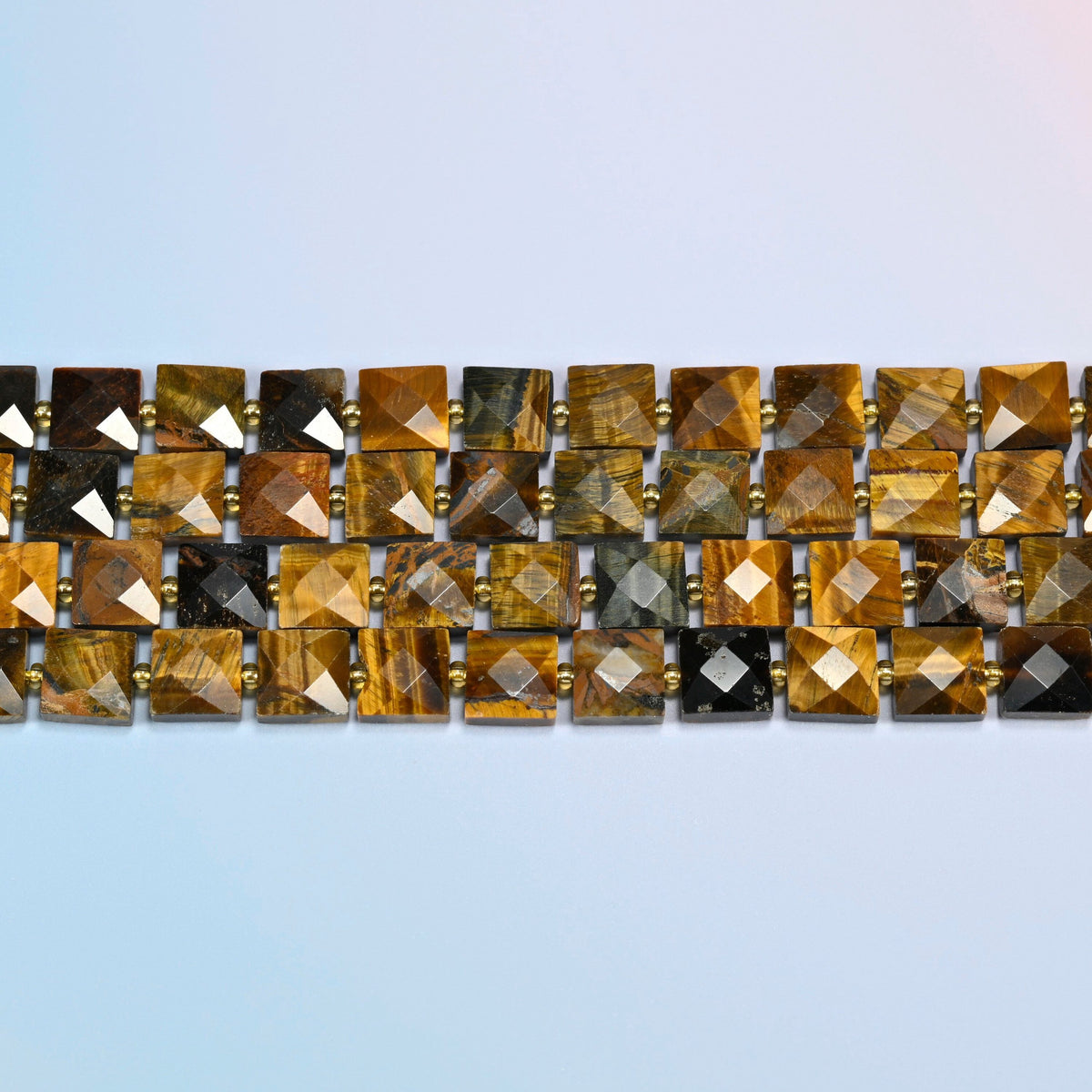Several strands of natural tiger eye faceted flat square beads laid in straight rows