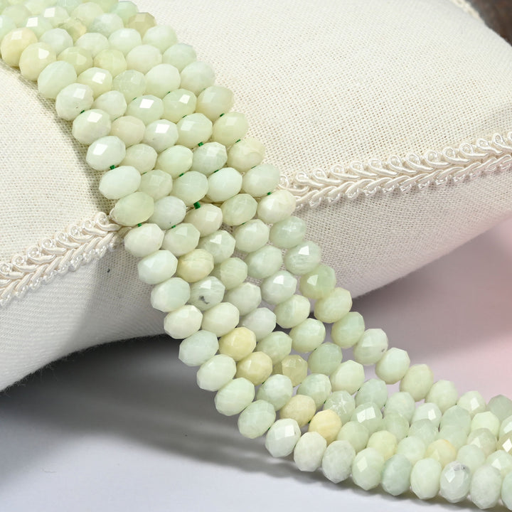 New jade faceted rondelle beads 5x8mm draped over a white cushion, soft green stone catching the light.