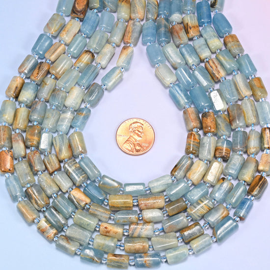 Bundled coil of faceted Blue Calcite tube beads on a lavender background with a penny placed at the center for scale.