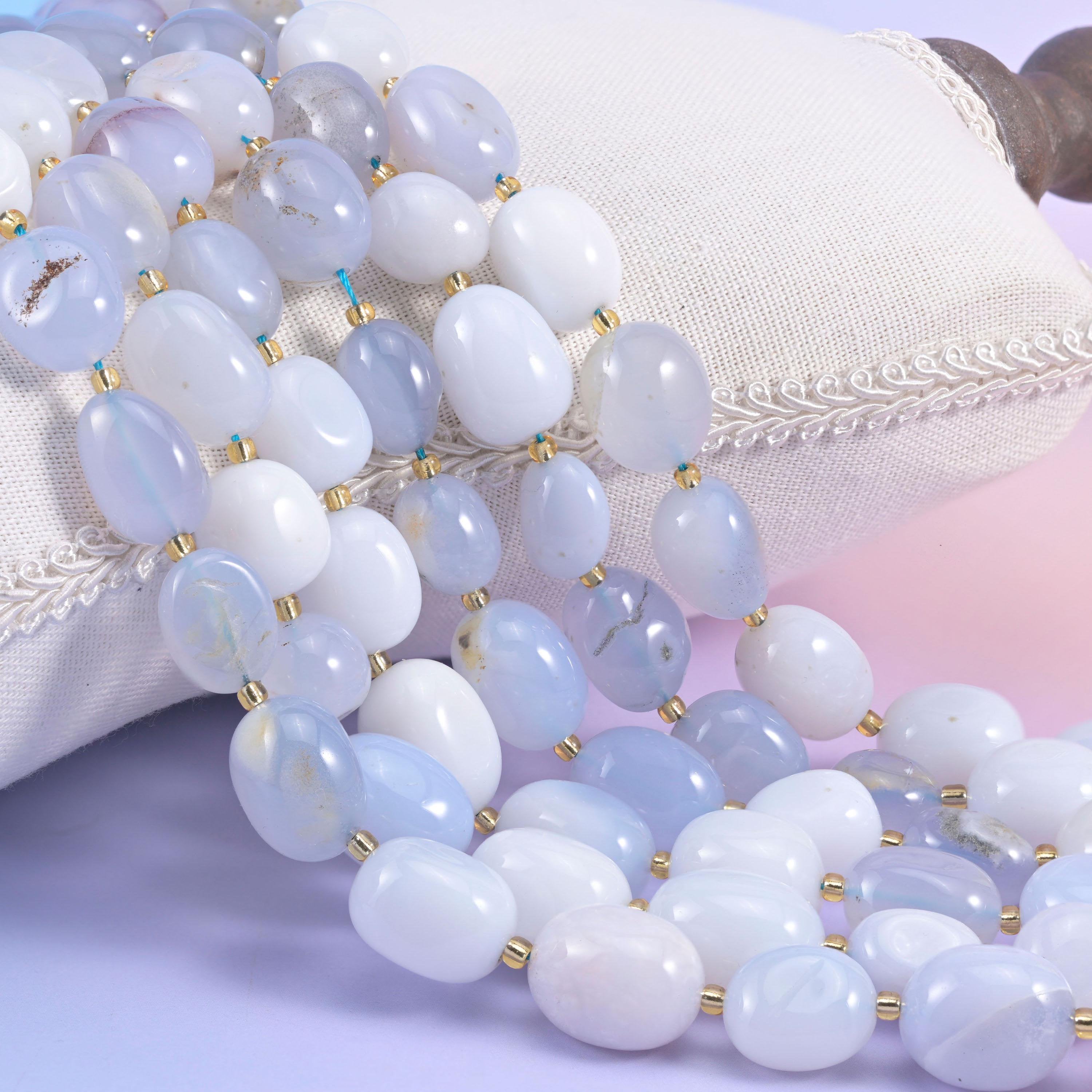Blue and white chalcedony nugget oval strands resting over a white cushion, milky and powder blue tumbled beads