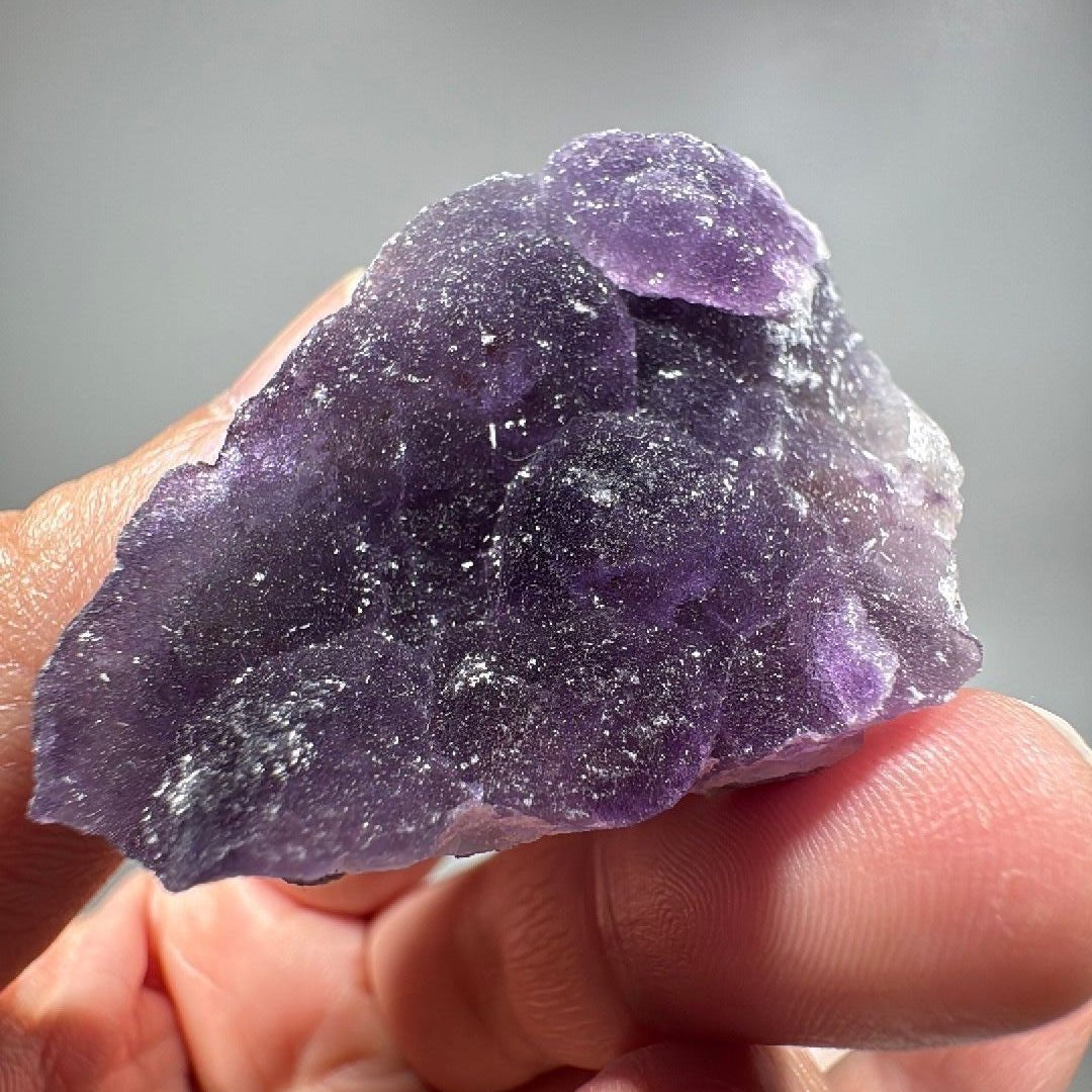 Hand holding a slab of deep purple fluorite with a fine sugary surface texture