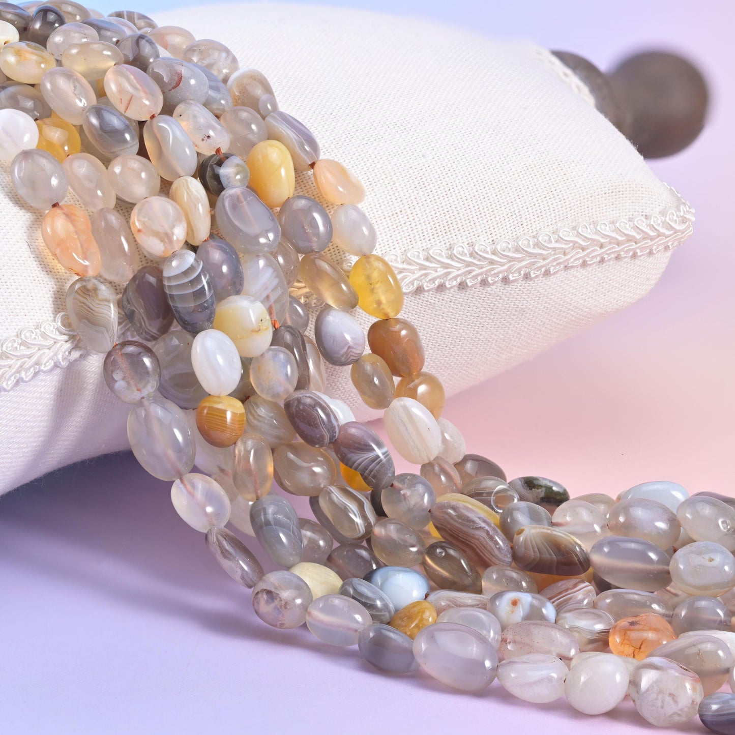Banded grey and cream Botswana Agate nugget strands beside a white cushion