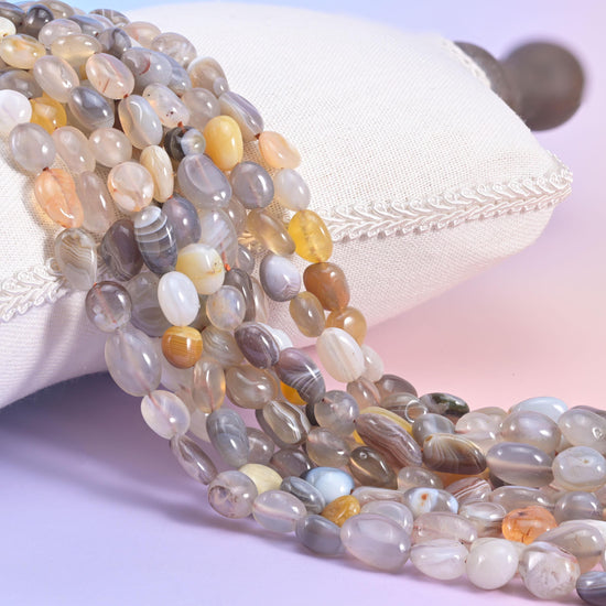 Banded grey and cream Botswana Agate nugget strands beside a white cushion