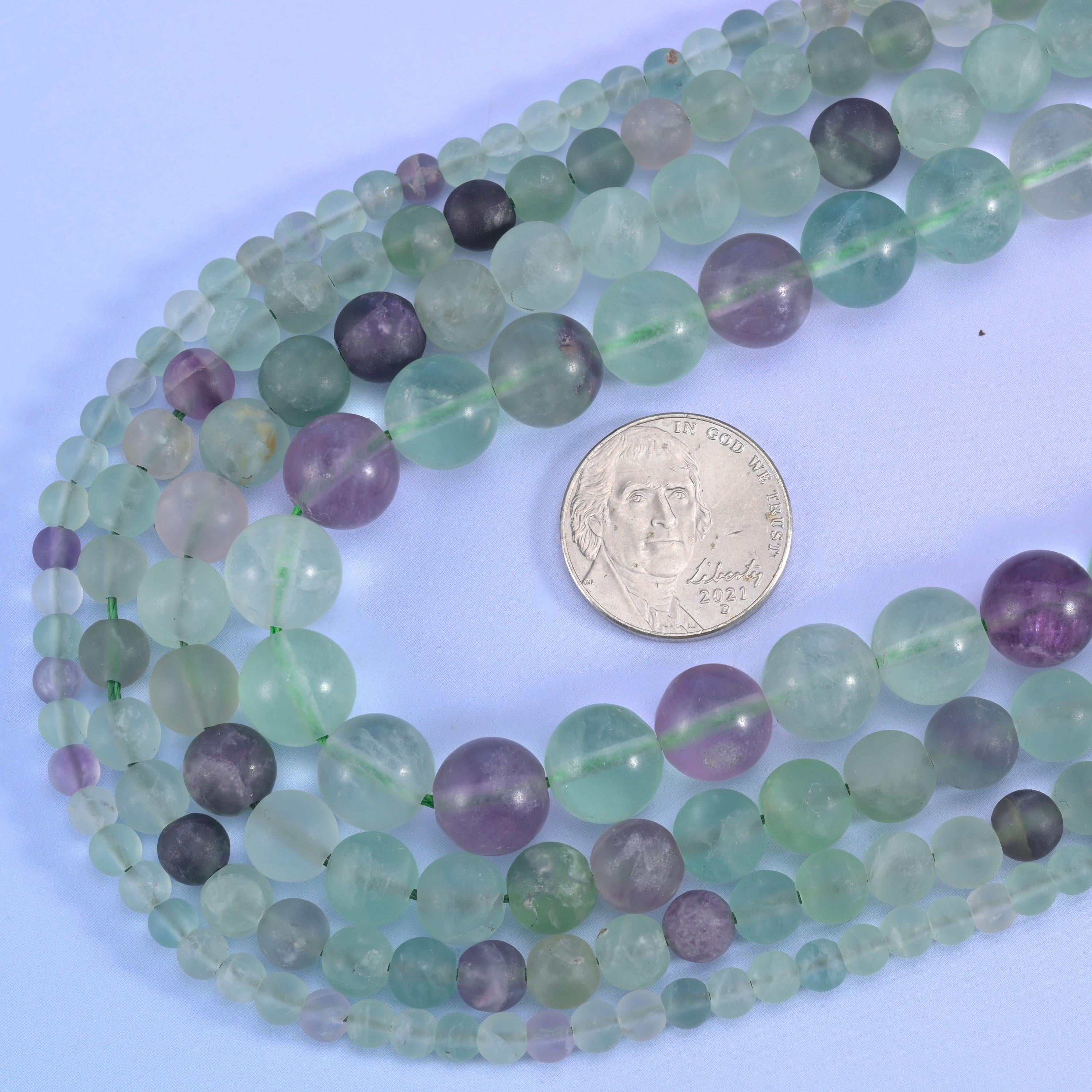 Frosted, non-shiny rounds banded in seafoam green, violet purple and near-clear white, the matte surface softening the colour into a sea-glass finish.