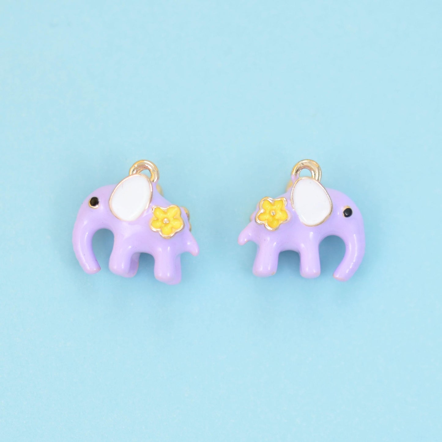 A little elephant in soft pastel enamel — dusty pink or lilac purple — with a cream-white ear, a dot of a dark eye and a…