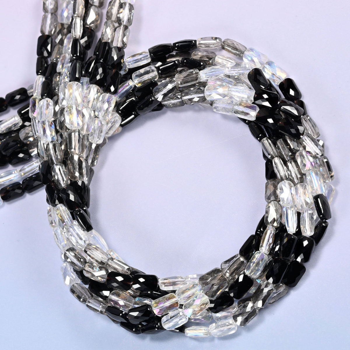 Black gray clear faceted rectangle glass beads coiled into a round loop against a purple background.