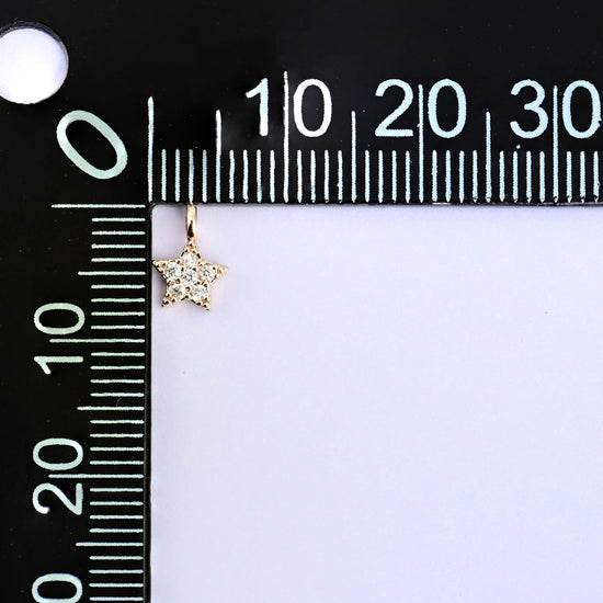 Small gold charms, one star charm at the corner of a millimetre ruler showing the size