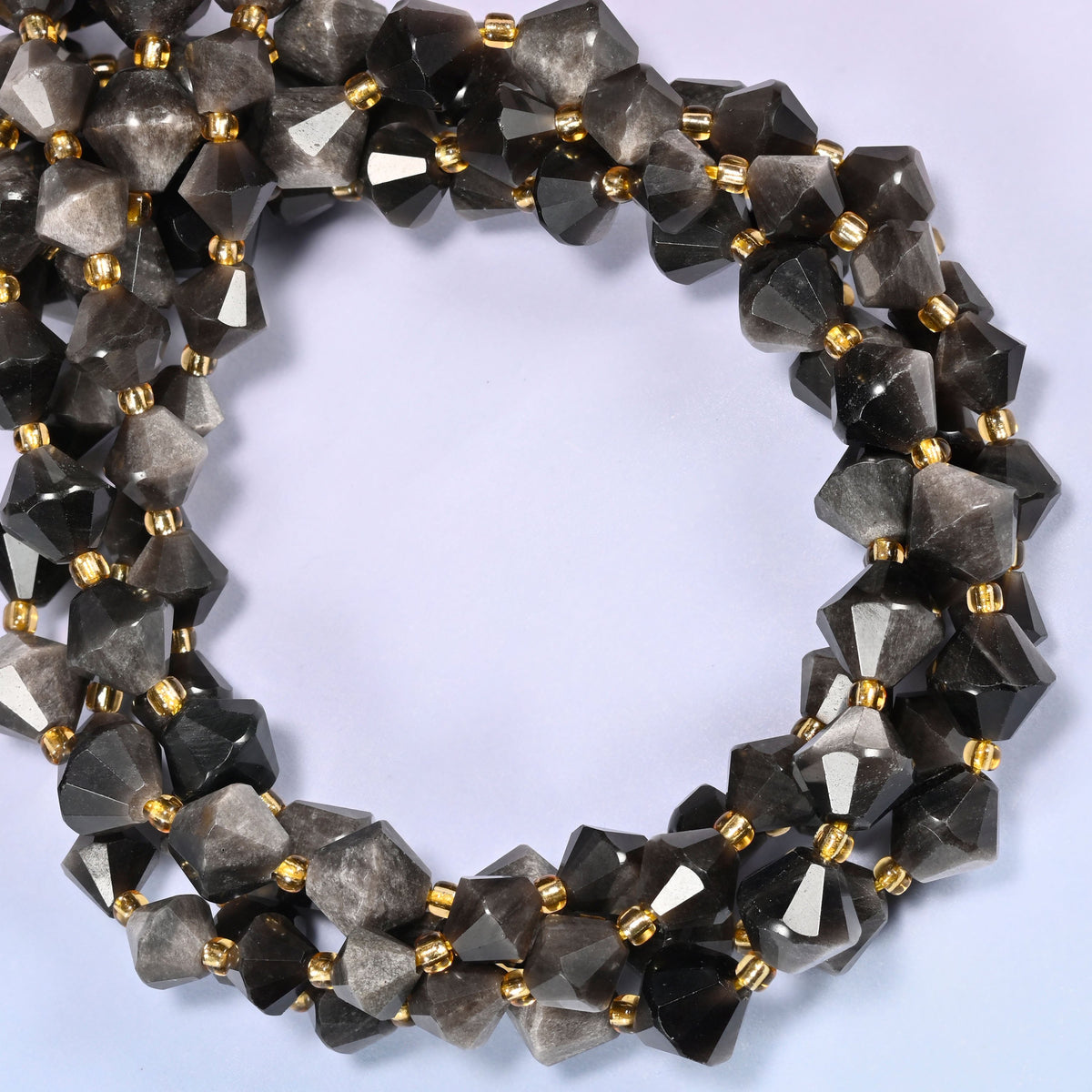 Silver obsidian bicone beads coiled into a round ring of several strands, a cool metallic glow traveling around the coil.