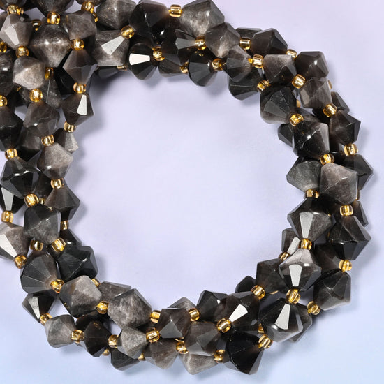 Silver obsidian bicone beads coiled into a round ring of several strands, a cool metallic glow traveling around the coil.