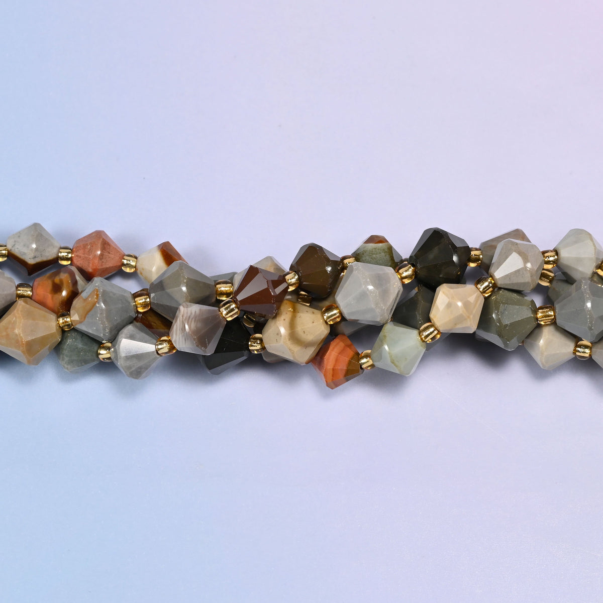 Macro close-up of American Picture Jasper faceted bicone beads on a strand, showing the faceted cut and gold-tone spacer beads.