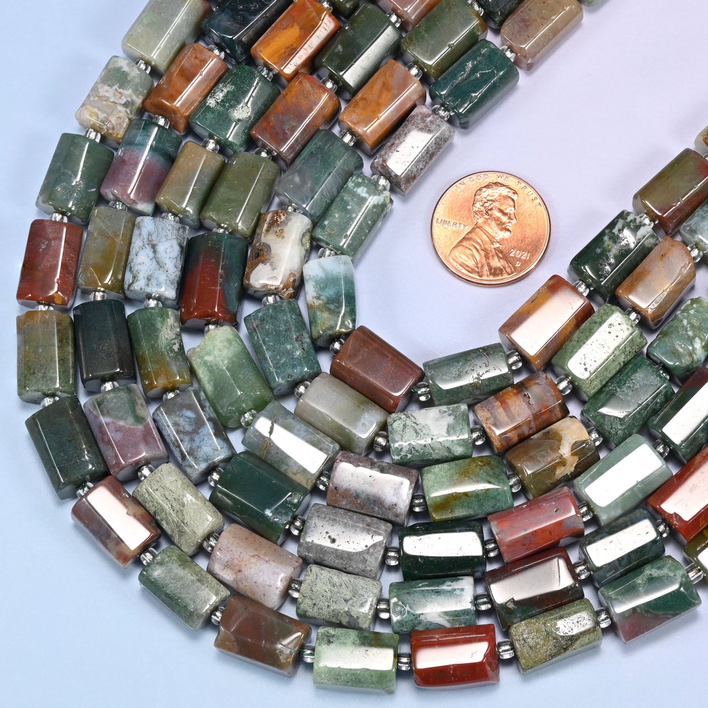 Coiled strands of faceted Indian Agate tube beads on a lavender surface with a US penny placed beside them for scale reference.