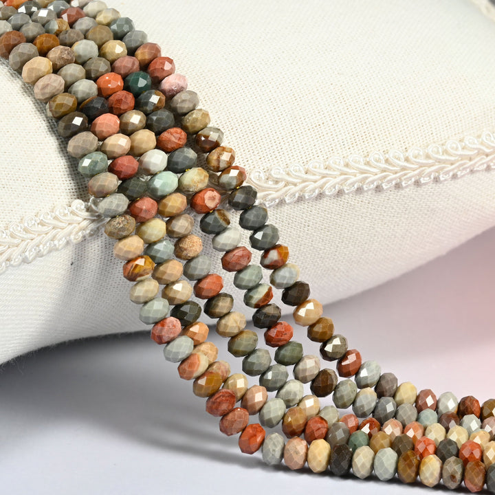 American Picture Jasper gemstone rondelle beads 4x6mm faceted, strand draped over a cream fabric cushion