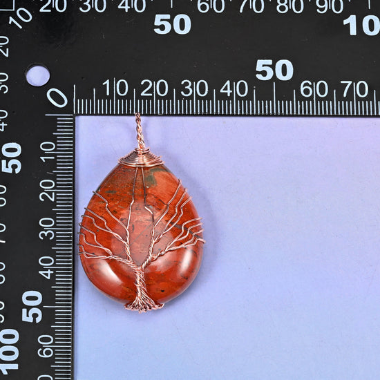 Teardrop Crystal Pendant with Copper Wired Tree measured against a black millimetre ruler, the red jasper piece running about 55x30mm.