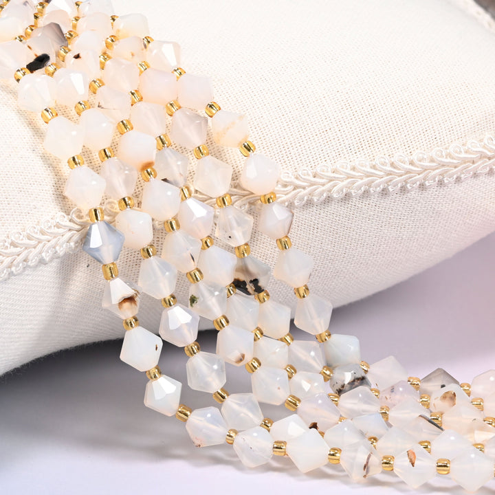 Black Flower Agate faceted bicone beads draped over a cushion, close-up of the black flower-like blooms and gold-tone spacers.